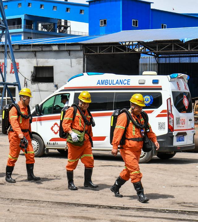 Rettungskräfte in orangenen Anzügen laufen vor einem Krankenwagen.