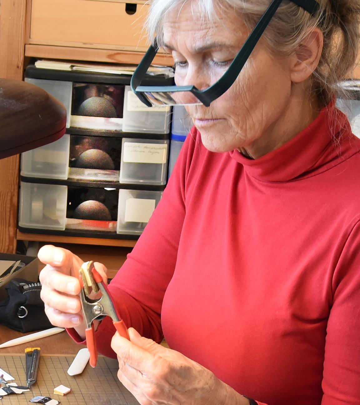 Die Miniaturbuchherstellerin Kathrin Hohensee arbeitet in ihrer Werkstatt an Puppenhausbüchern. In der Hand hält sie eine Zange mit einem der Mini-Bücher.