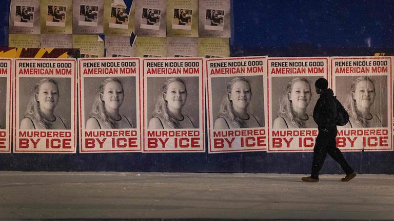 Eine Person läuft vor einer Reihe von Plakaten, auf denen "Renee Nicole Good, American Mom, Murdered by ICE" zu lesen ist.