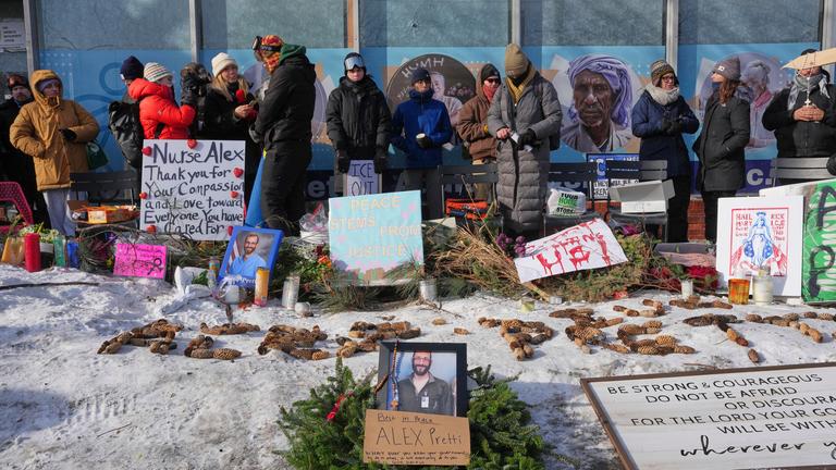 Menschen Gedenken einem Todesopfer in Minessota. Auf dem Boden sind Blumen und Bilder vom Opfer zu erkennen.