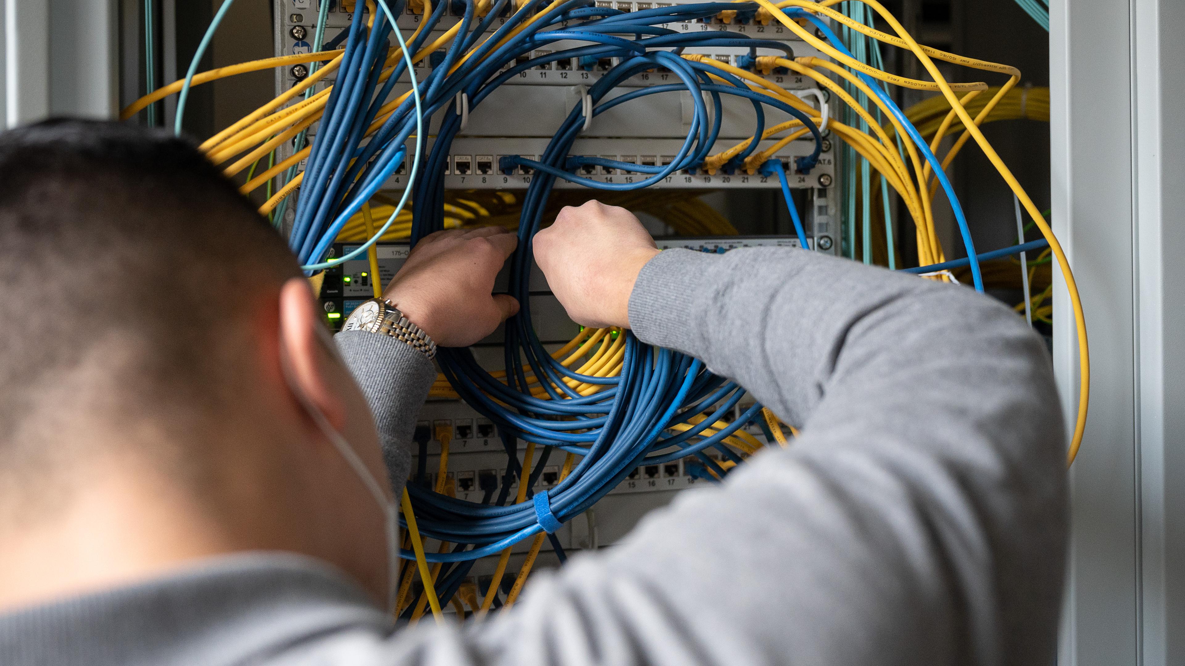  Ein Auszubildender Fachinformatiker Systemintegration steckt an einem Server ein Netzwerkkabel ein.