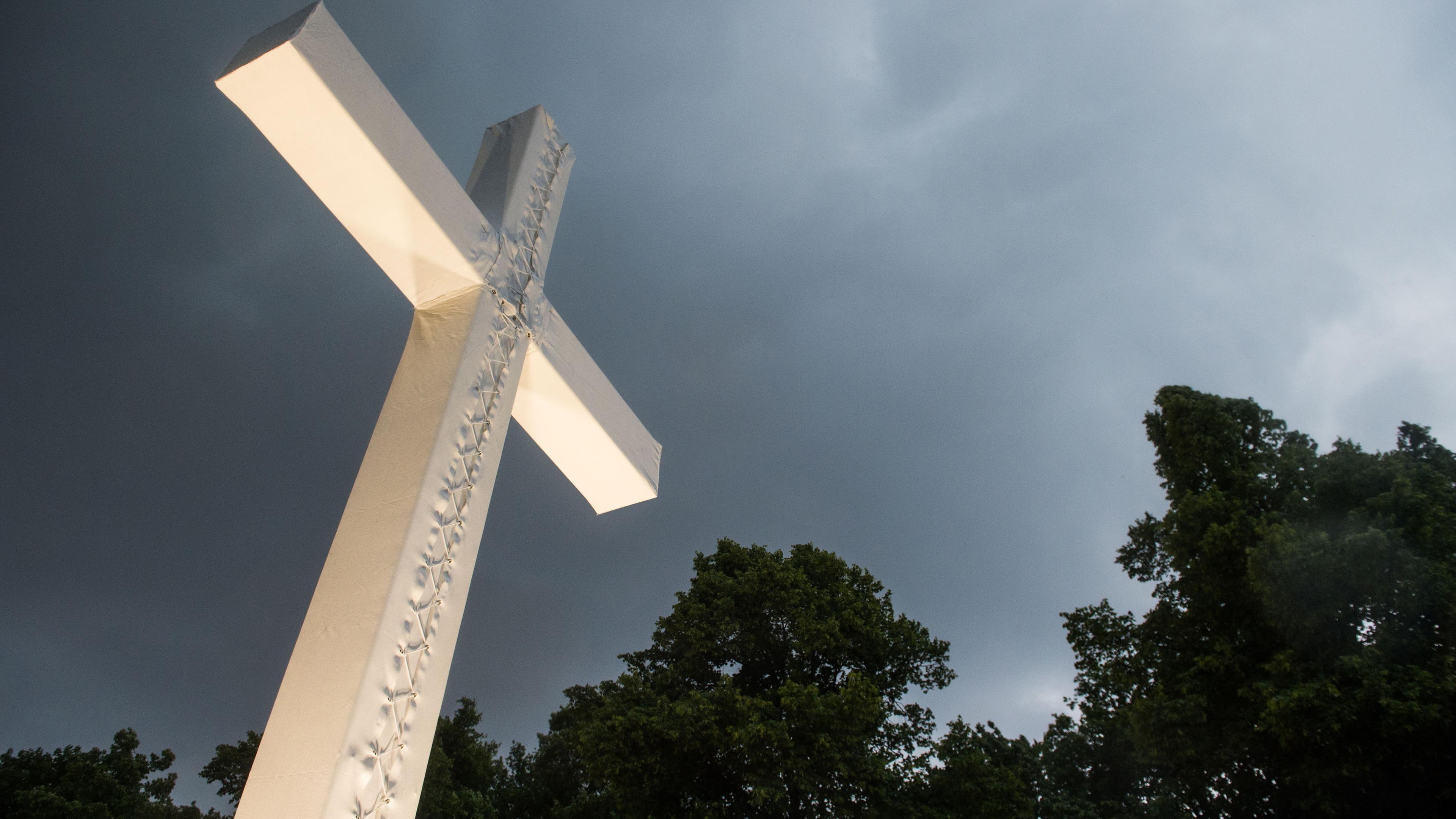 Berlin: Dunkle Wolken ziehen über einem überdimensionierten Kreuz auf. (Symbolbild)