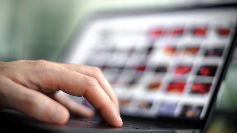 Die Finger einer Hand auf dem Tastatur eines geöffneten Laptops.