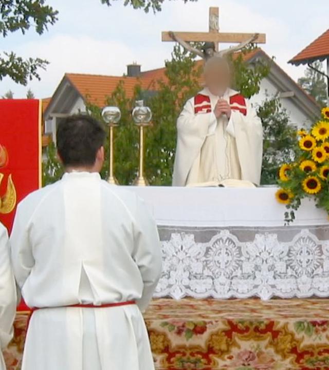 Screenshot aus Video: Eine Andacht im Freien, ein Pfarrer in der Bildmitte (Gesicht verpixelt), Messdiener im Vordergrund