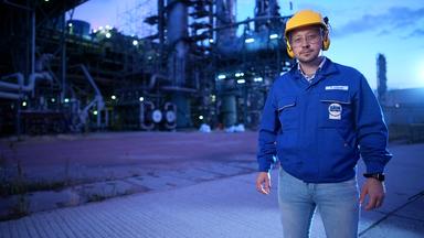 Ein Mann in blauer Arbeitsjacke vor einer Fabrik