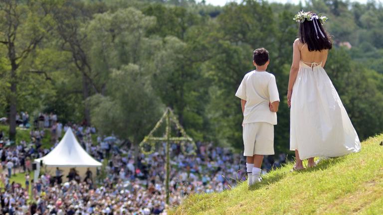 Menschen feiern Mittsommer mit Tänzen rund um den Maibaum auf dem Gelände von Schloss und Gärten Gunnebo in Mölndal bei Göteborg, Schweden.