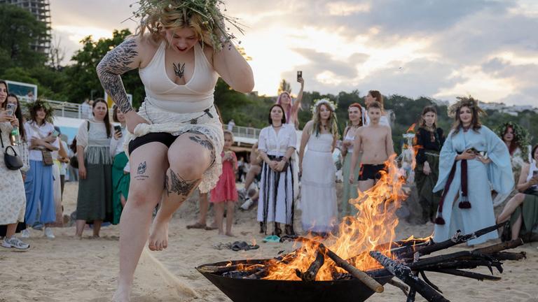 Eine Frau mit Blumenkranz springt während der Feierlichkeiten zum traditionellen Ivan-Kupala-Fest über ein Lagerfeuer an einem Strand in Odesa. Das Fest zur Sommersonnenwende hat in der Ukraine vorchristliche Wurzeln.