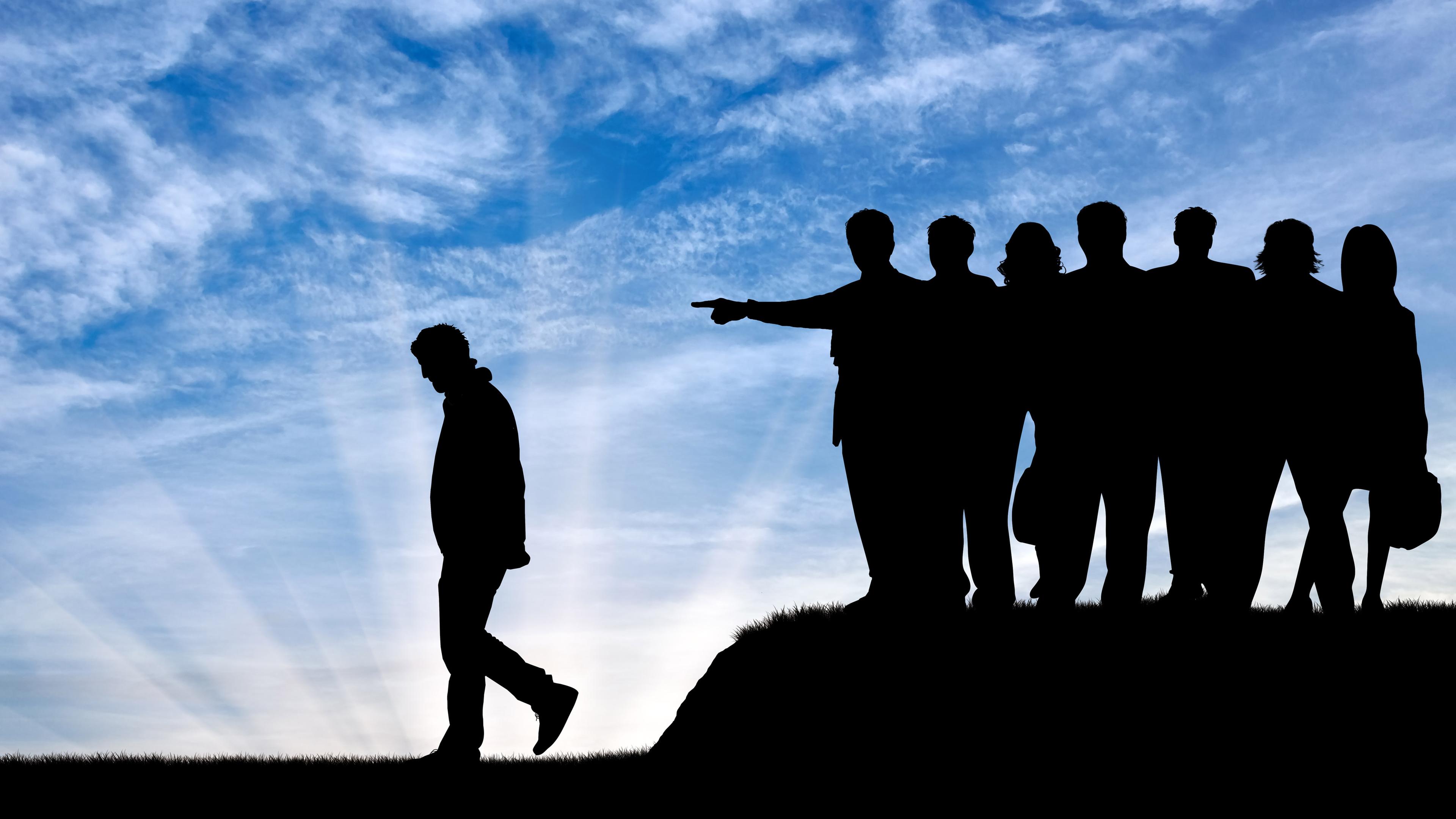 Eine Person wendet sich von einer Gruppe ab. Eine Person aus der Gruppe zeigt mit dem Arm in die entgegengesetzte Richtung, um die Einzelperson auszugrenzen.