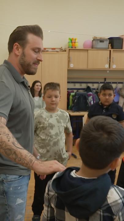Daniel Duddek steht mit Jeans und Polohemend in Kreis von Kindern. 
