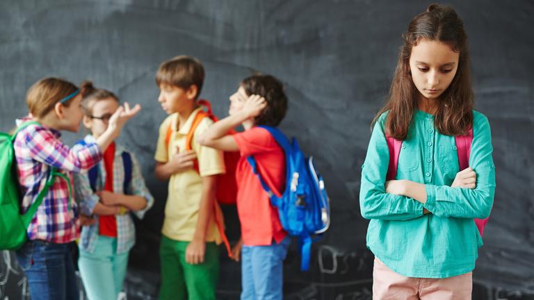 Ein besorgtes Mädchen steht alleine neben ihren Klassenkameraden.