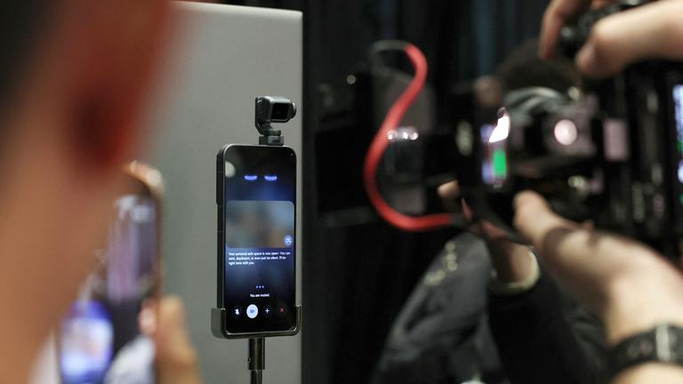 Eine verschwommene Kamera im Vordergrund wird auf ein fokussiertes Handy gehalten, das auf dem Mobile World Congress ausgestellt ist.