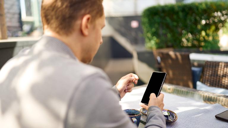 Ein Mann sitzt im Freien und schaut auf sein Smartphone.