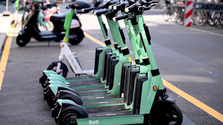 Eine Reihe von E-Rollern stehen auf einem Stellplatz an der Straße. 