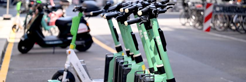 Eine Reihe von E-Rollern stehen auf einem Stellplatz an der Straße. 