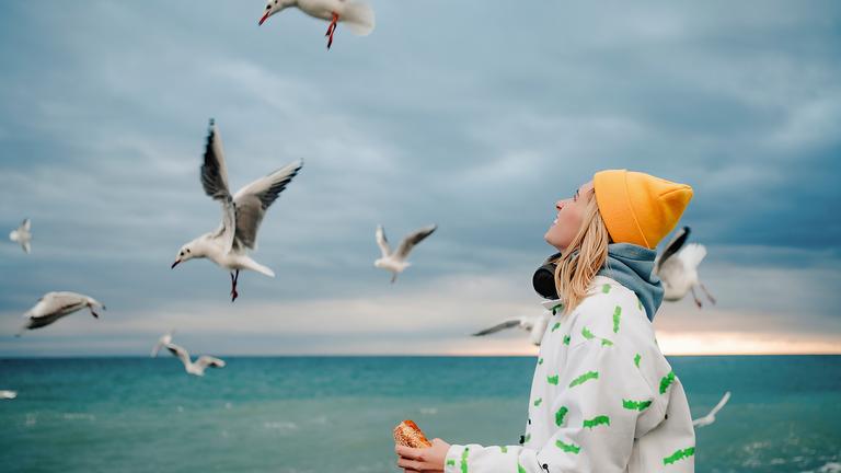 Eine junge Frau füttert Möwen, die am Ufer schweben