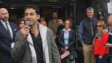 Mohsen Mahdawi hält ein Mikrofon in der Hand, um ihn herum stehen mehrere Menschen.