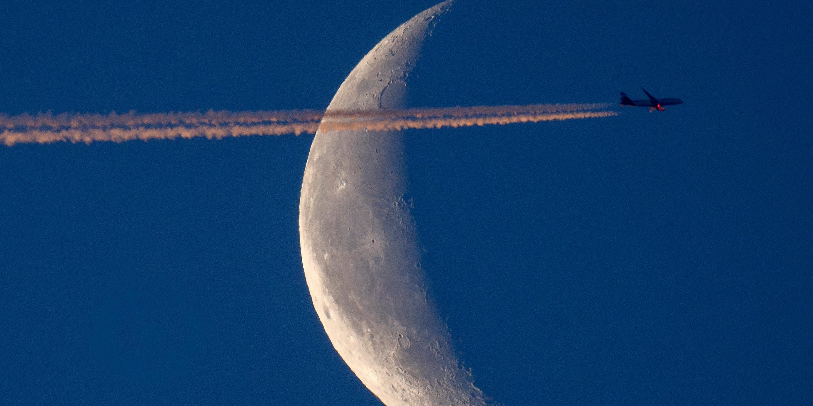 Ein Flugzeug fliegt über Frankfurt, im Hintergrund ist der Mond zusehen. (Archiv)