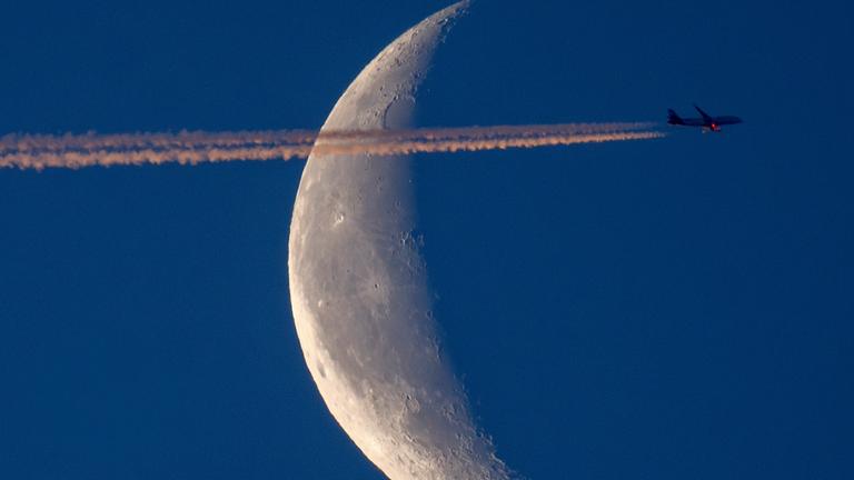 Ein Flugzeug fliegt über Frankfurt, im Hintergrund ist der Mond zusehen. (Archiv)