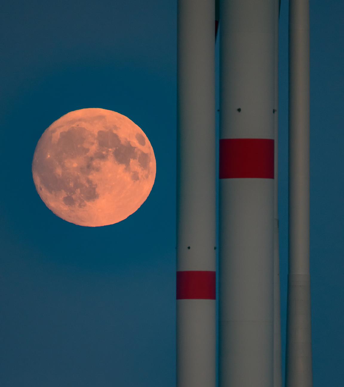 Der zunehmende Mond ist kurz nach seinem Aufgang in Sieversdorf, Brandenburg, neben den Masten von Windenergieanlagen zu sehen. 