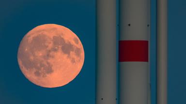 Der zunehmende Mond ist kurz nach seinem Aufgang in Sieversdorf, Brandenburg, neben den Masten von Windenergieanlagen zu sehen. 
