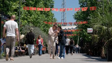 Fußgänger gehen am 18.05.2026, in Montenegros Hauptstadt Podgorica, auf einer mit Nationalflaggen geschmückten Straße spazieren. 