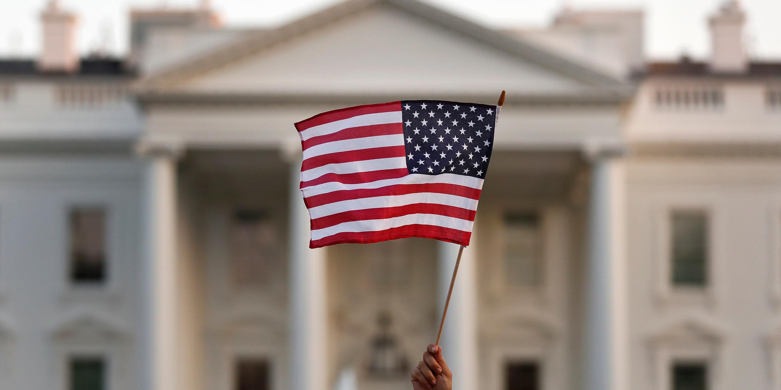 Eine USA-Flagge weht im wind und wird vor dem Weißen Haus in Washington hochgehalten.