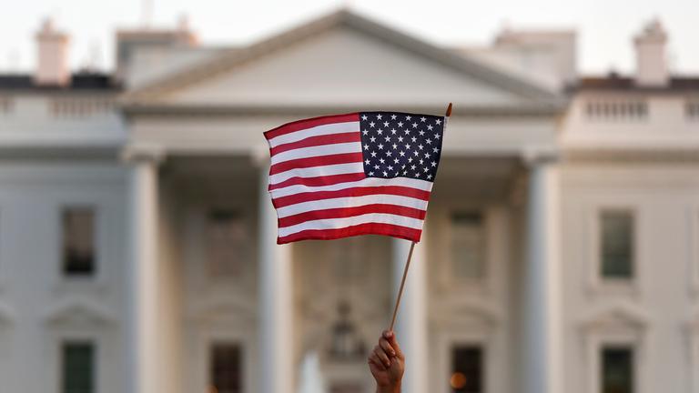 Eine USA-Flagge weht im wind und wird vor dem Weißen Haus in Washington hochgehalten.