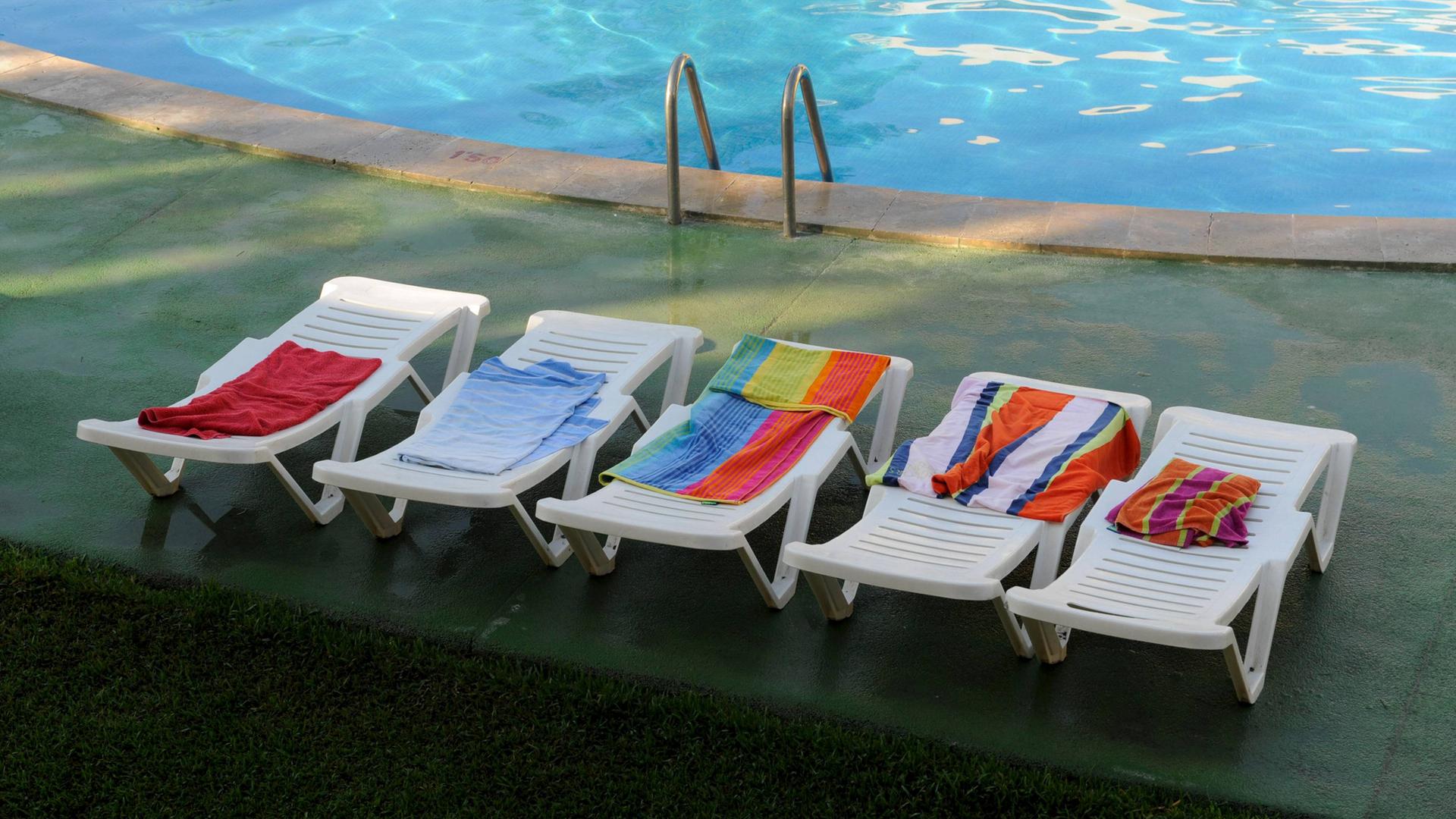 Leere, reservierte Sonnenliegen an einem Hotel-Pool in Spanien.