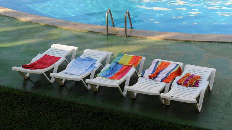 Leere, reservierte Sonnenliegen an einem Hotel-Pool in Spanien.