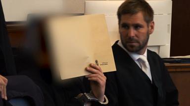 Ein Mann sitzt im Gerichtssaal und versteckt sein Gesicht hinter einer Mappe.