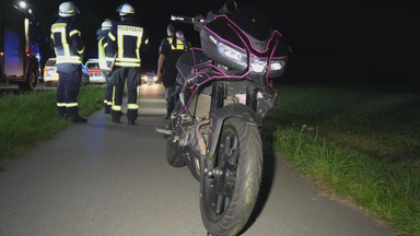 Das Bild zeigt ein Motorrad. Im Hintergrund sind Einsatzkräfte der Feuerwehr zu sehen.