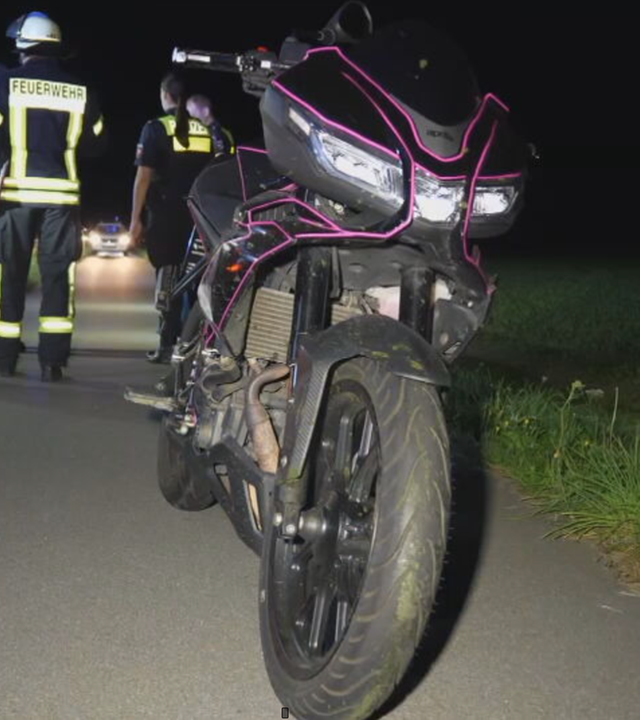 Das Bild zeigt ein Motorrad. Im Hintergrund sind Einsatzkräfte der Feuerwehr zu sehen.