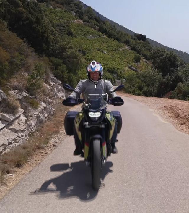 Der Reporter fährt auf dem Motorrad durch die Berge.