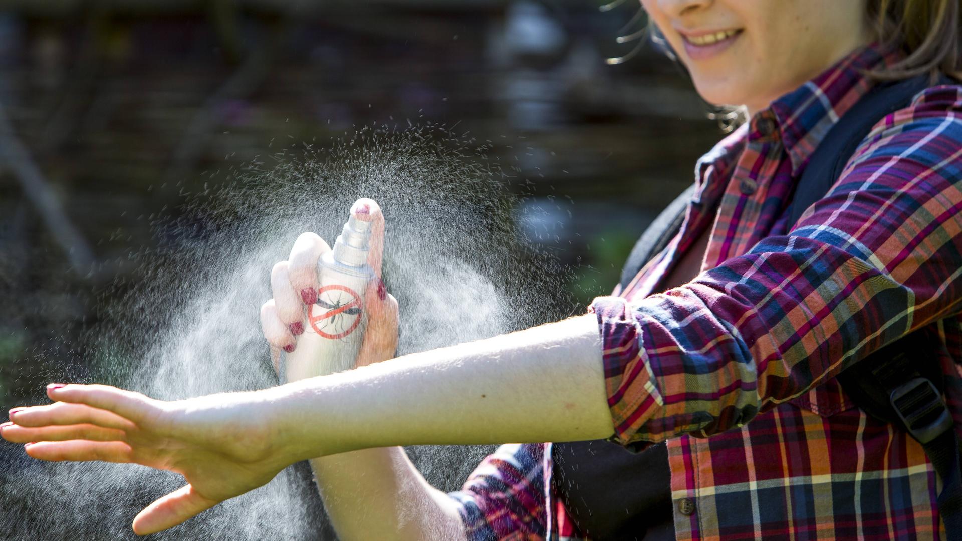 Frau trägt Mückenschutzspray auf dem Unterarm auf.