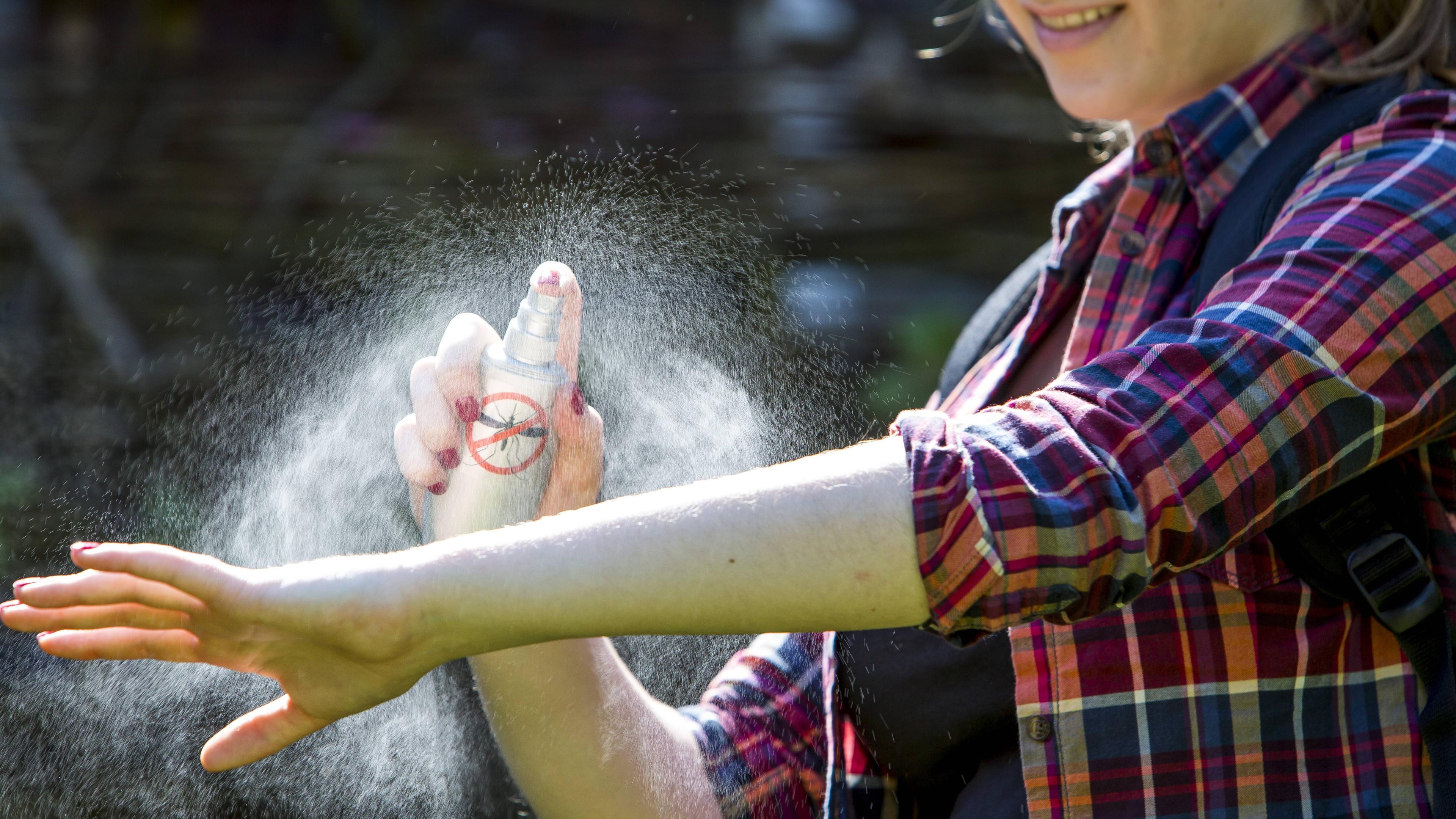 Frau trägt Mückenschutzspray auf dem Unterarm auf.
