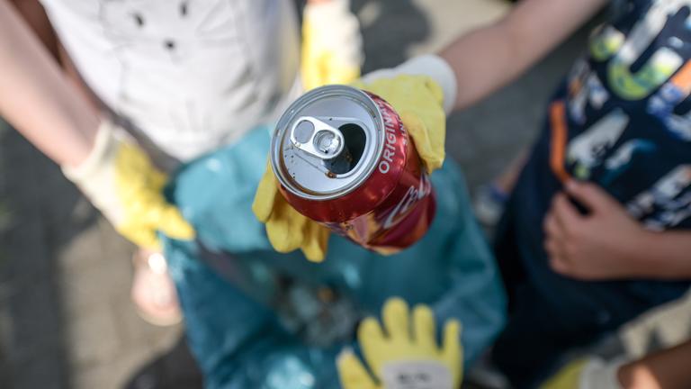 Eine Gruppe Müllsammler wirft eine Pfanddose in einen Müllsack.