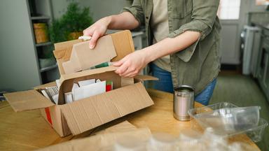 Eine Frau sortiert Kartons, Papier, Konservendosen und Plastikverpackungen an einem Tisch in ihrer Wohnung.