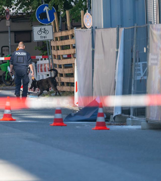  Ein Polizist mit einem Polizei-Spürhund läuft an einem Firmengelände vorbei. 