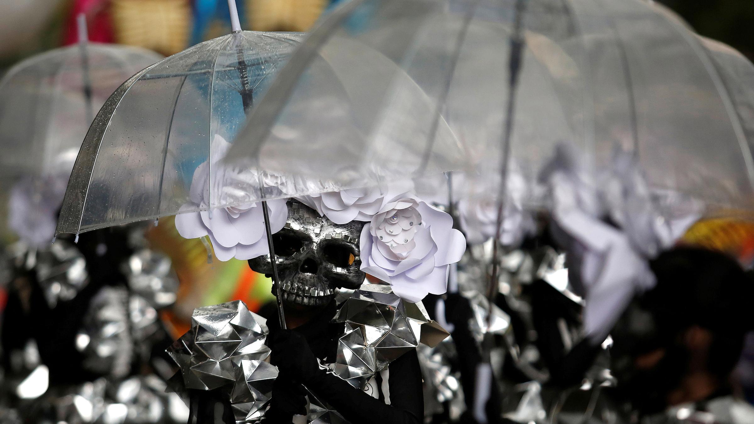 Eine Gruppe mit Totenkopfmasken unter Regenschirmen beim day of the dead in Mexiko City