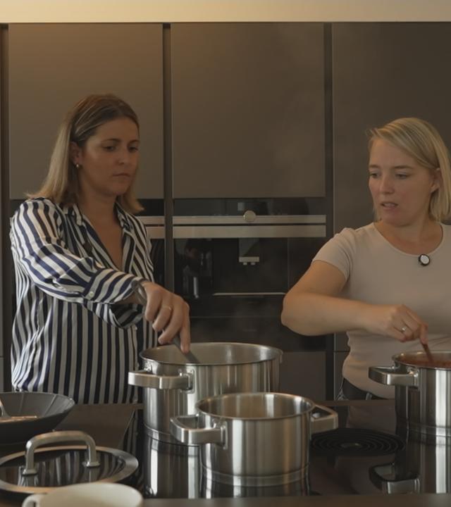 Eine Mütterpflegerin unterstützt eine junge Mutter beim Kochen