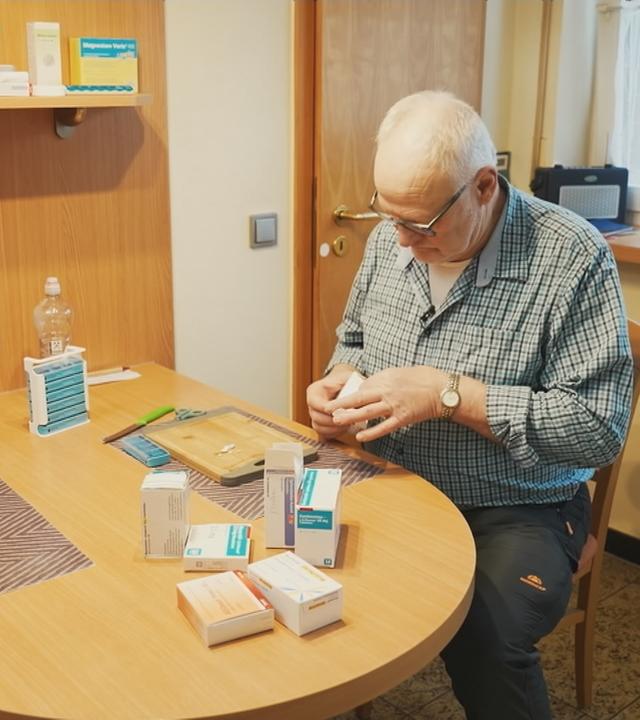 Mann sitzt am Tisch und sortiert seine Medikamente