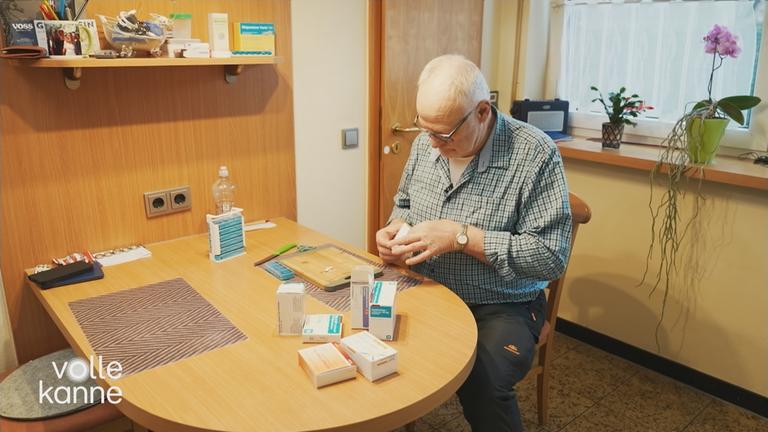 Mann sitzt am Tisch und sortiert seine Medikamente