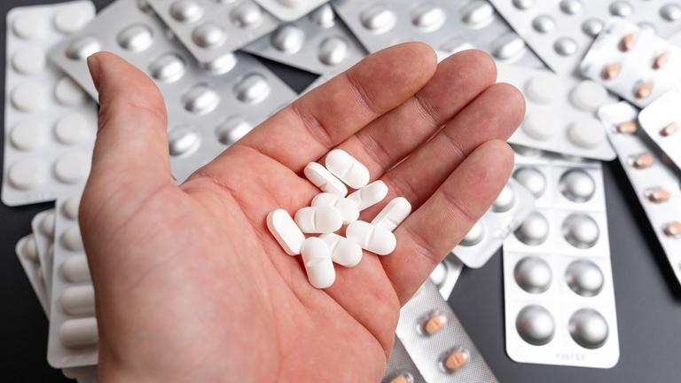 Eine Hand hält viele Tabletten, im Hintergrund sind Blister zu sehen.