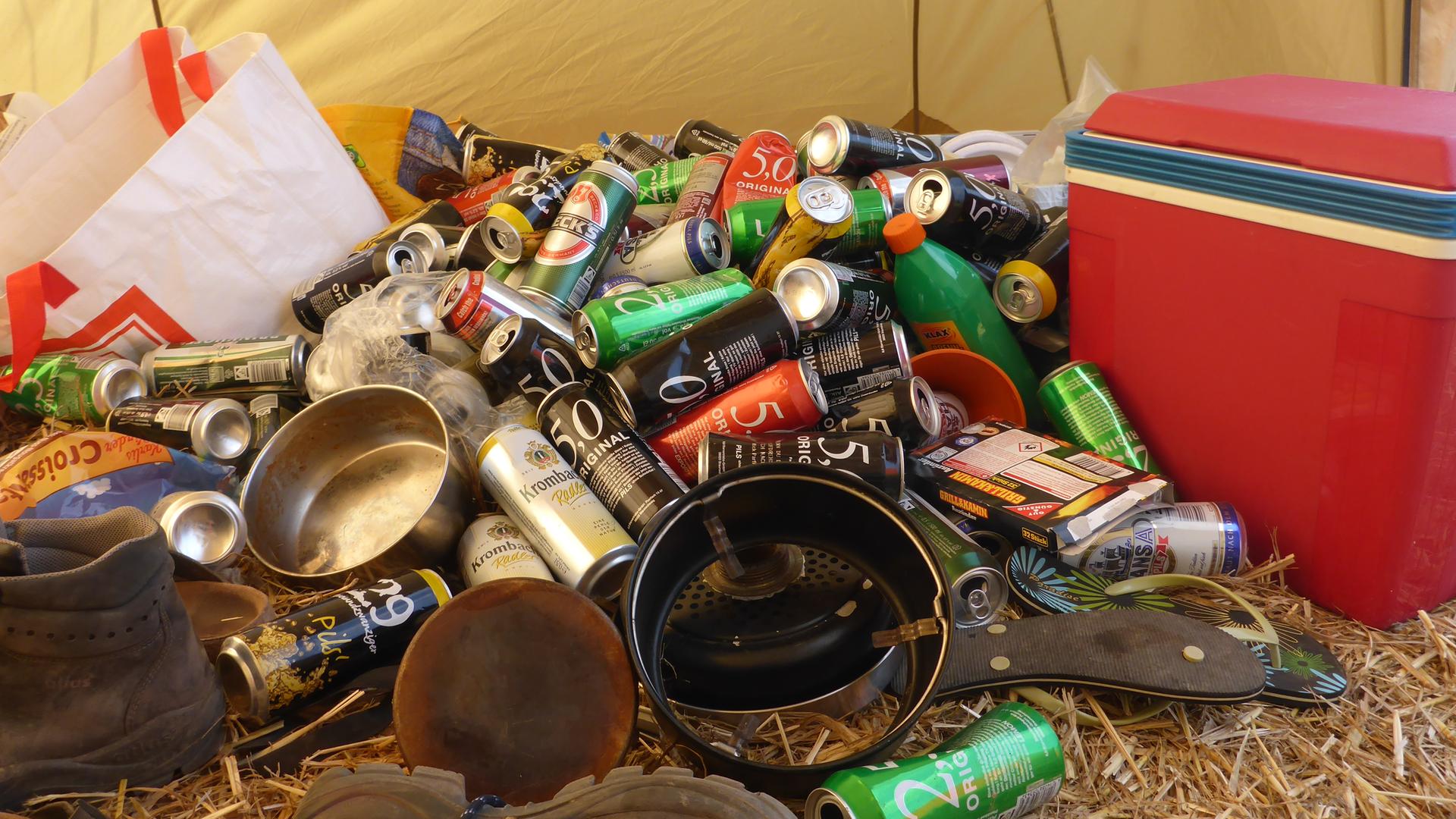 Im Innenraum eines Zeltes liegen jede Menge leere Dosen, Geschirr, Schuhe und eine Kühlbox.