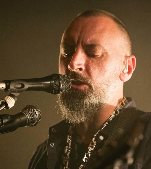 Ein Mann mit graumeliertem Bart singt in Mikrofone.