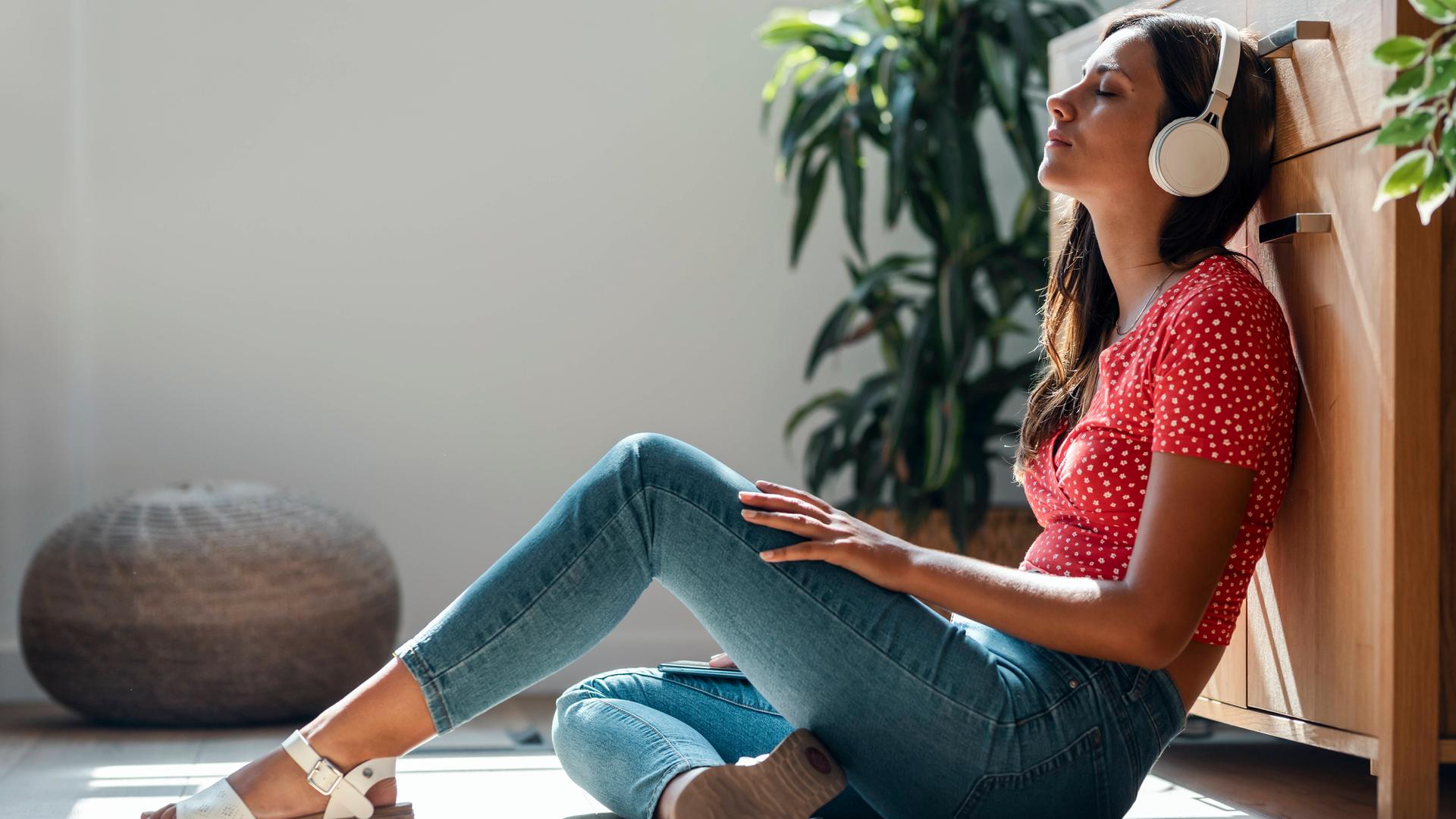 Eine junge Frau sitzt mit Kopfhörer auf dem Boden und entspannt.