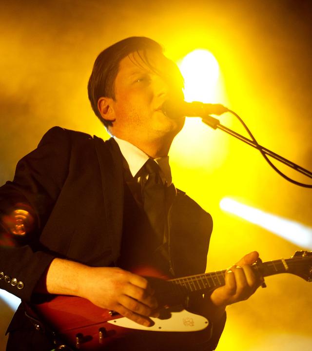 Ein Mann, der E-Gitarre spielt, singt in ein Mikrofon.