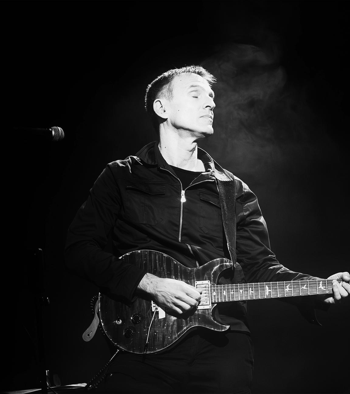 Man sieht eine Schwarz-Weiß-Fotografie auf der ein Mann zu sehen ist, der E-Gitarre spielt.