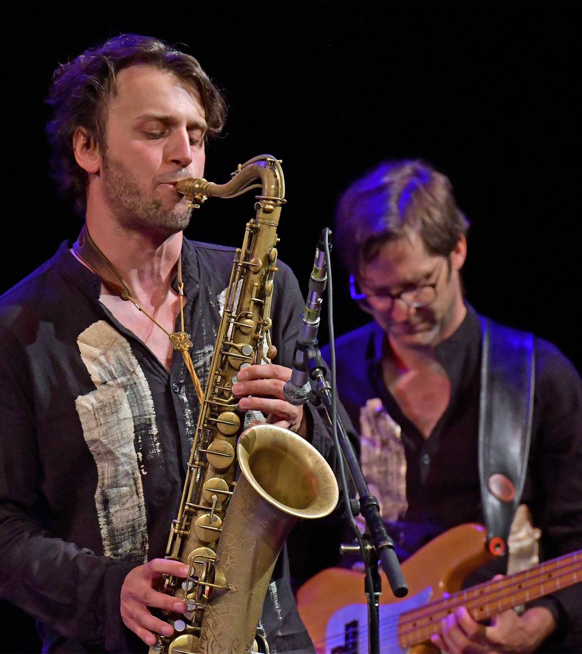 Ein Saxophonist und ein Bassist spielen auf einer Bühne.
