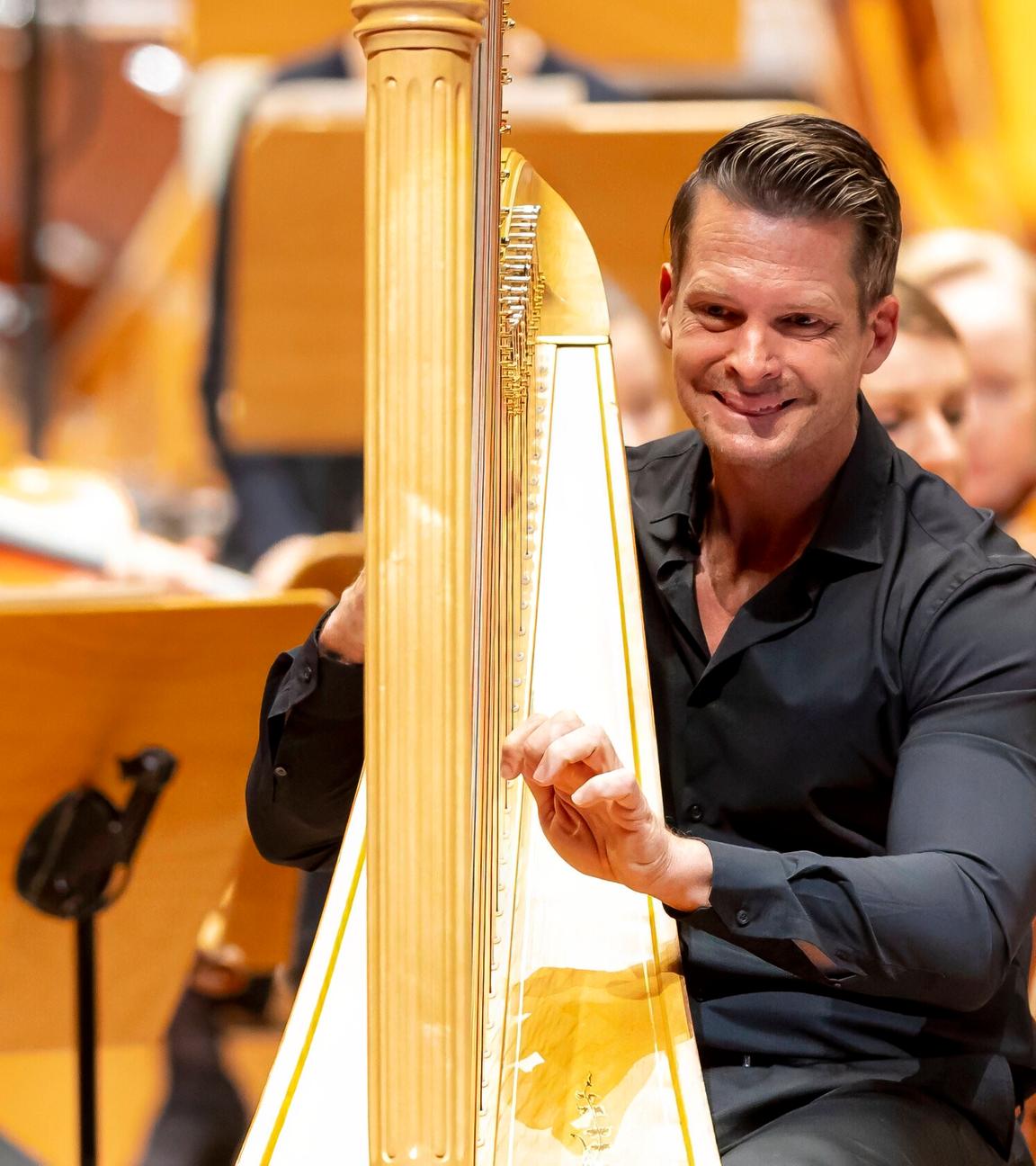 Ein Mann spielt auf einer Harfe, umgeben von einem Orchester.